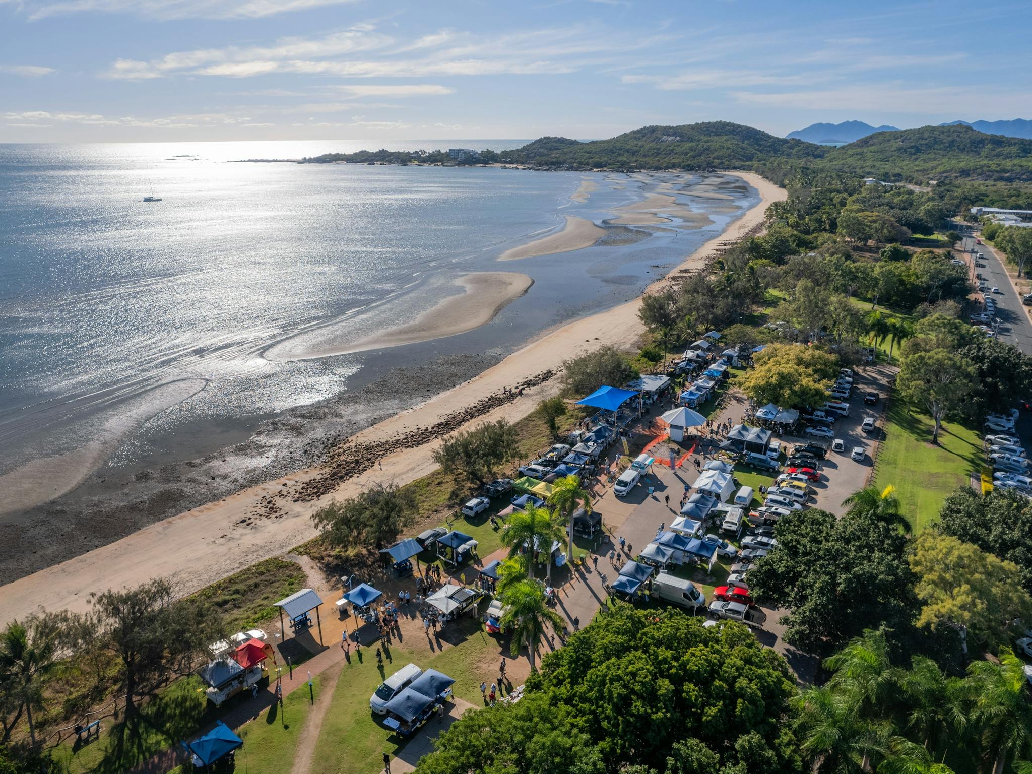 Aerial view of the market stalls and cars along a beautiful beach, greenery and calm ocean waters Aerial view of the market stalls and cars along a beautiful beach, greenery and calm ocean waters