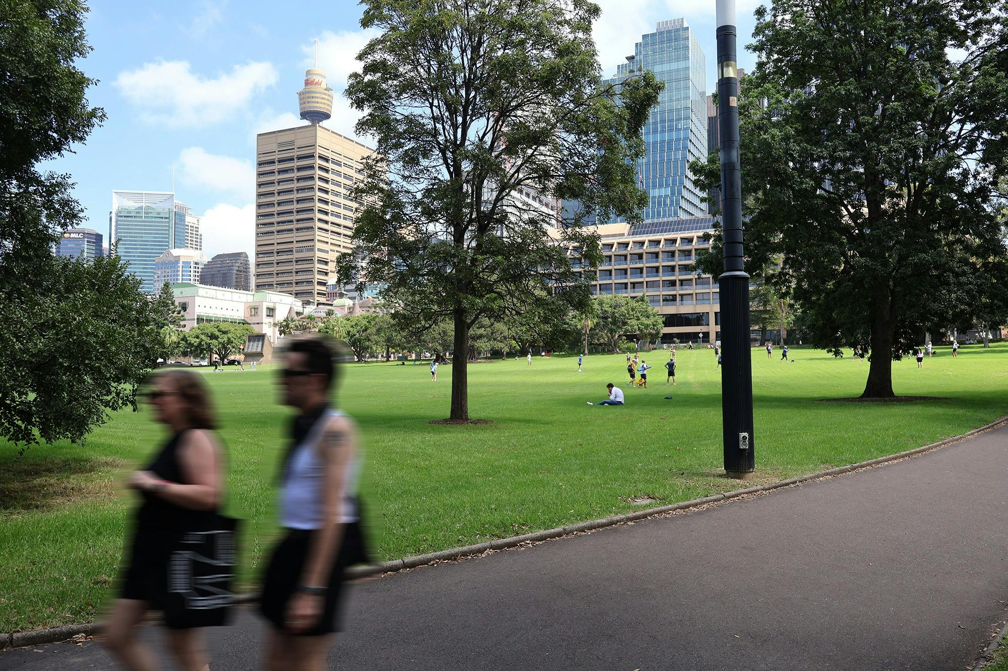 A park with lush green grass and two people walking on a path