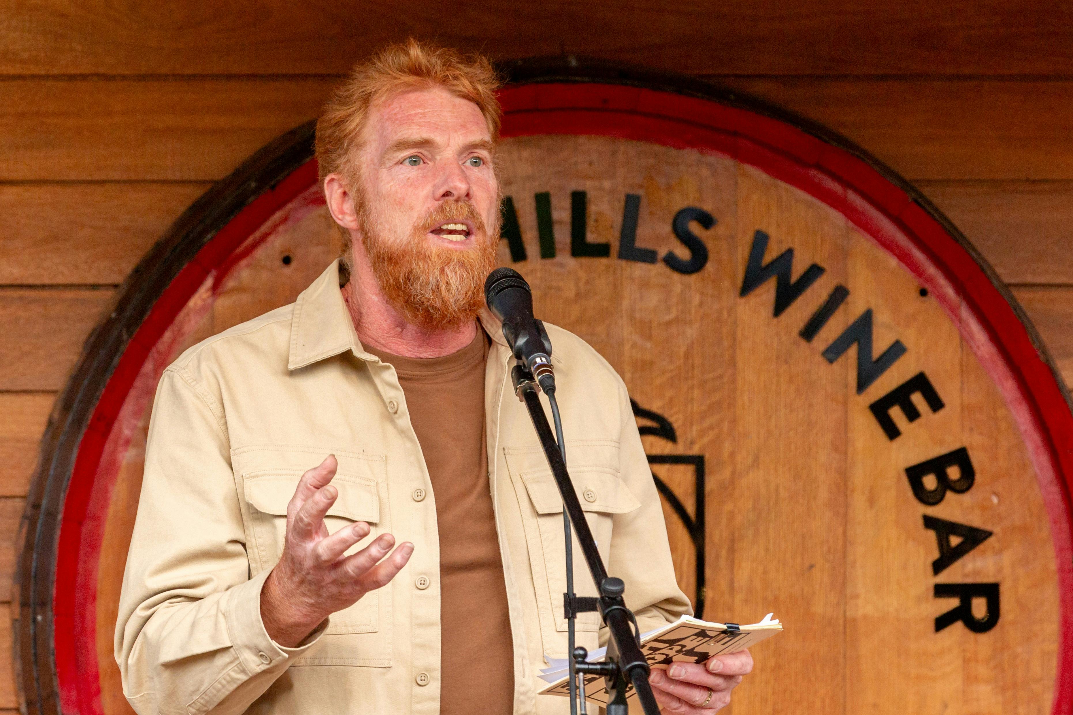 Man standing in front of a microphone, in front of Adelaide hills Wine Bar Branded barrel