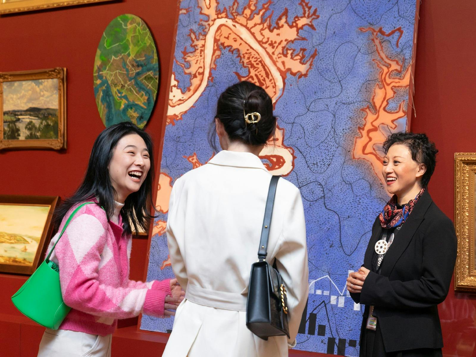 Three people stand in a gallery space talking and laughing.