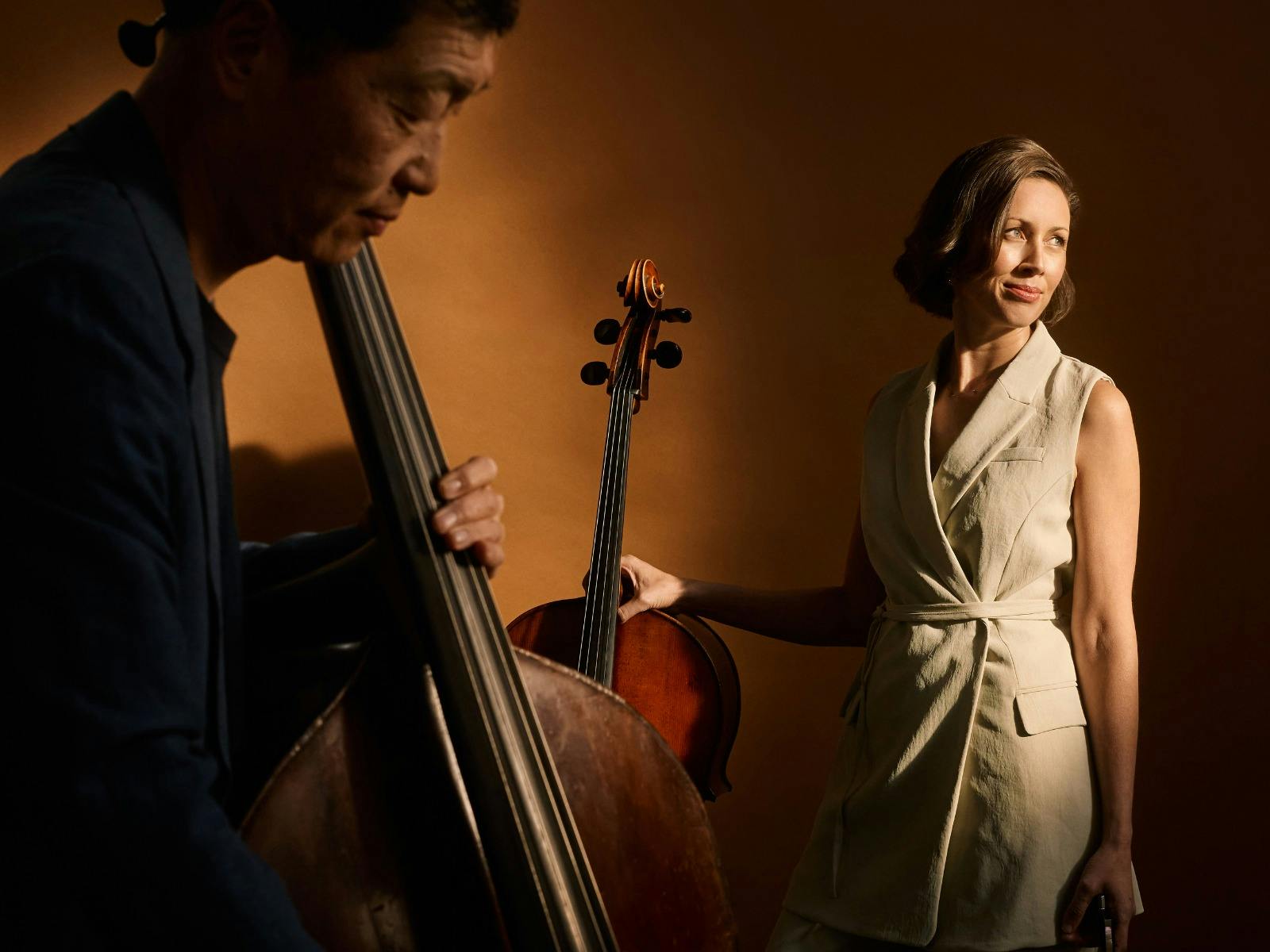 A photo of two orchestra players in a studio setting. Double bass foreground, cello background