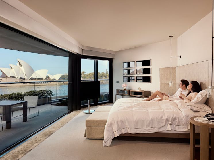 Couple enjoying the spectacular views of Sydney Harbour from their bedroom at the Park Hyatt