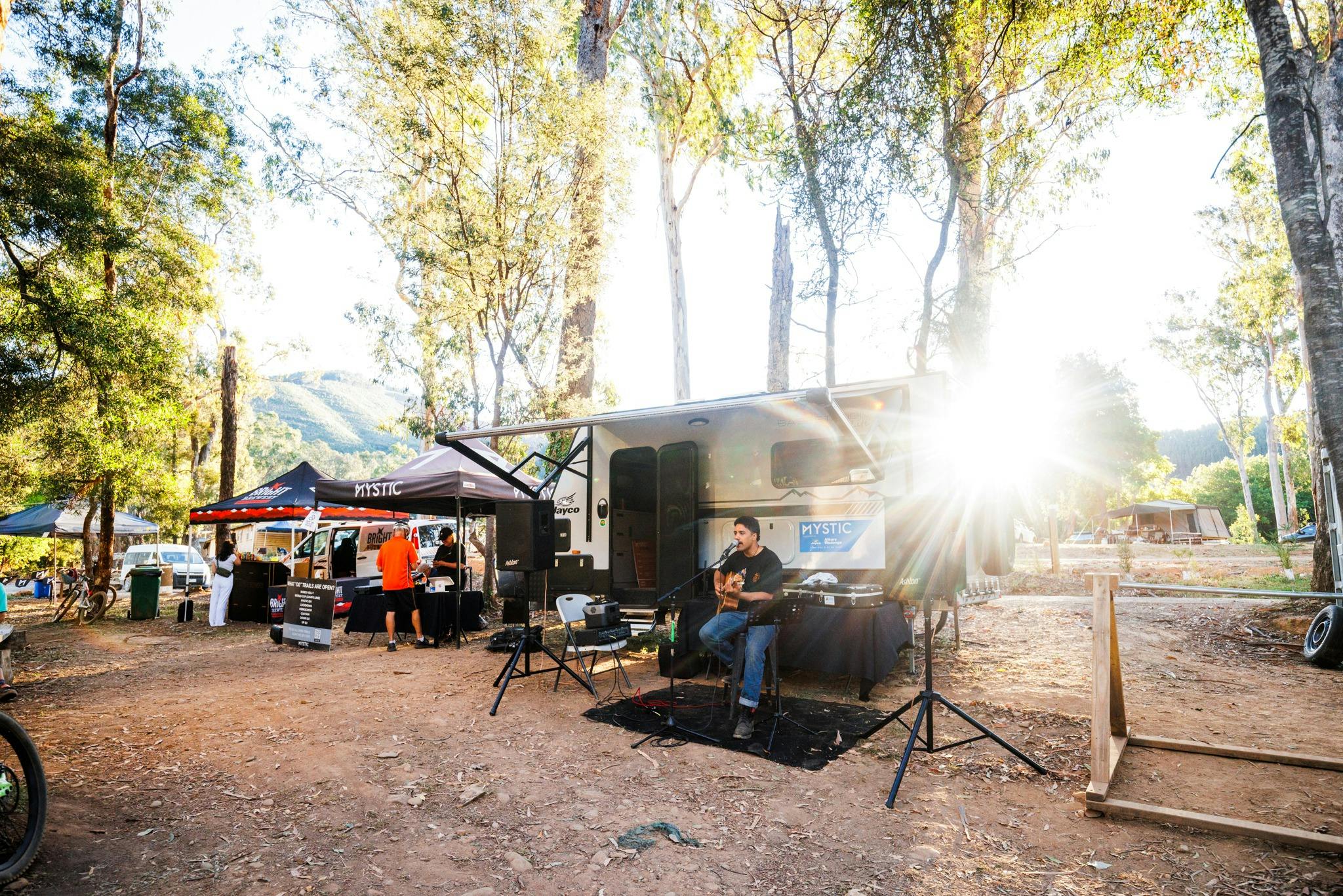 Caravan set up with music speakers and musician with sunset in background