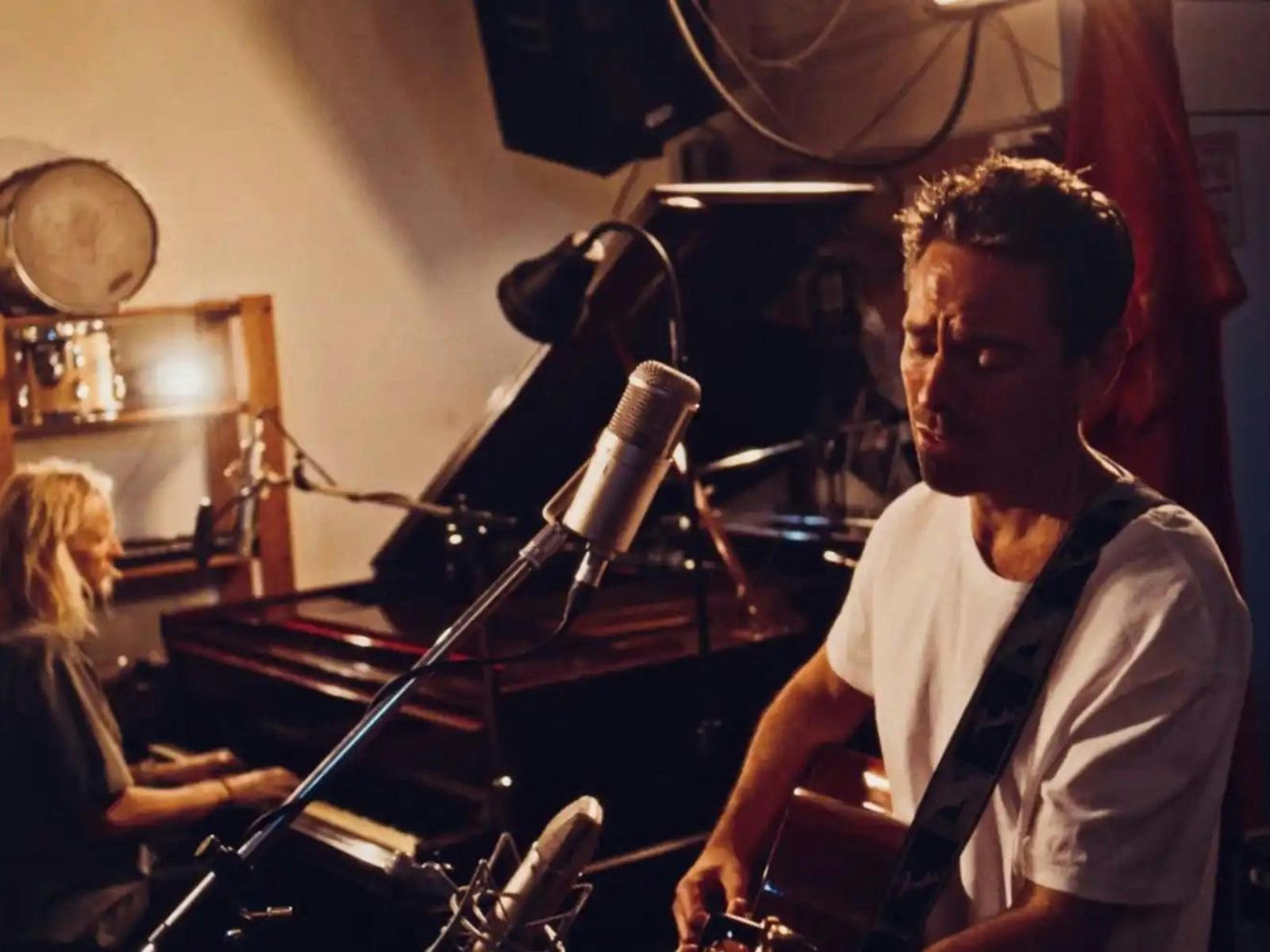 a man playing the guitar with a female playing the piano on the background