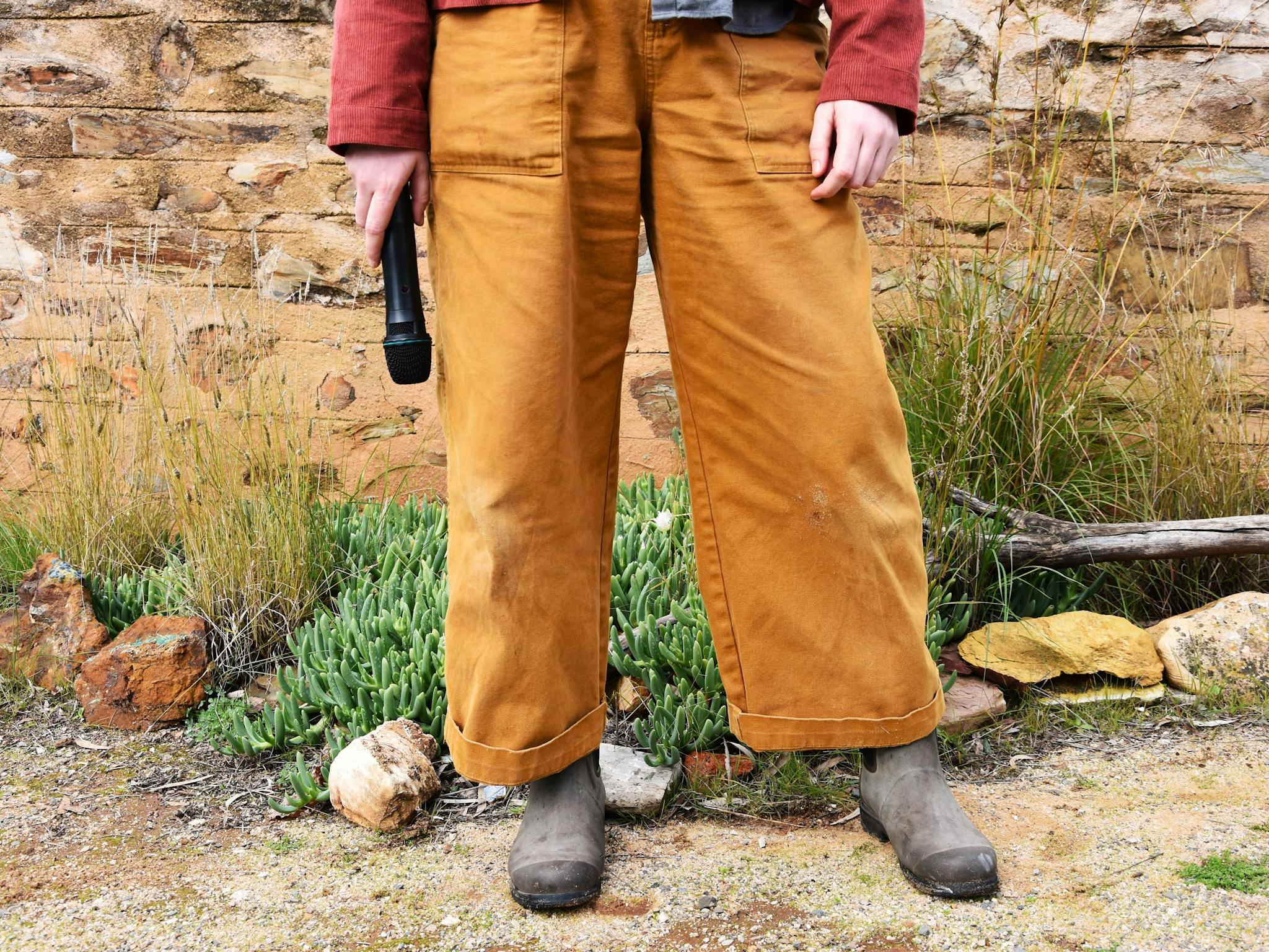 the lower half of a person wearing mustard yellow gardening pants/gumboots. They hold a microphone