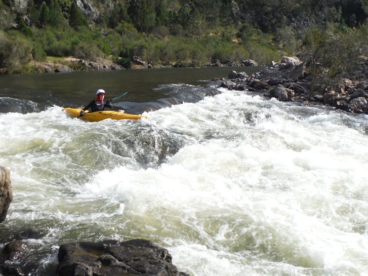 A boiling water rapid on the snowy river with a kayaker in a yellow about to enter the rapid