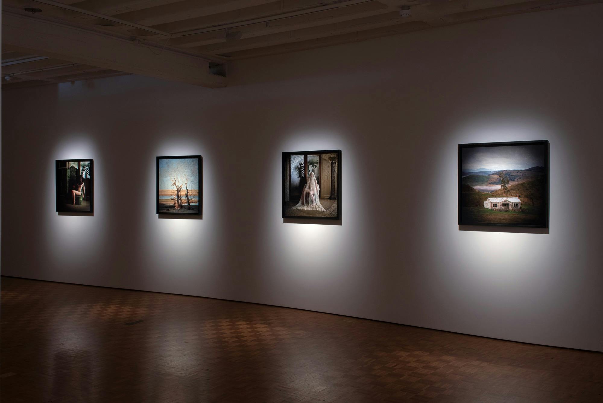 Four photographs depicting landscapes and portraits hang in a darkened gallery space.