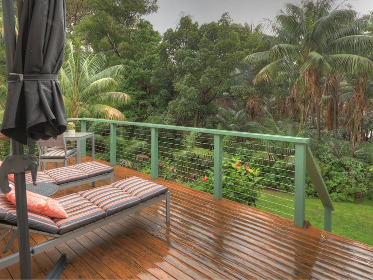 a veranda at Admiralty Apartments with lounges overlooking green scenery and rain
