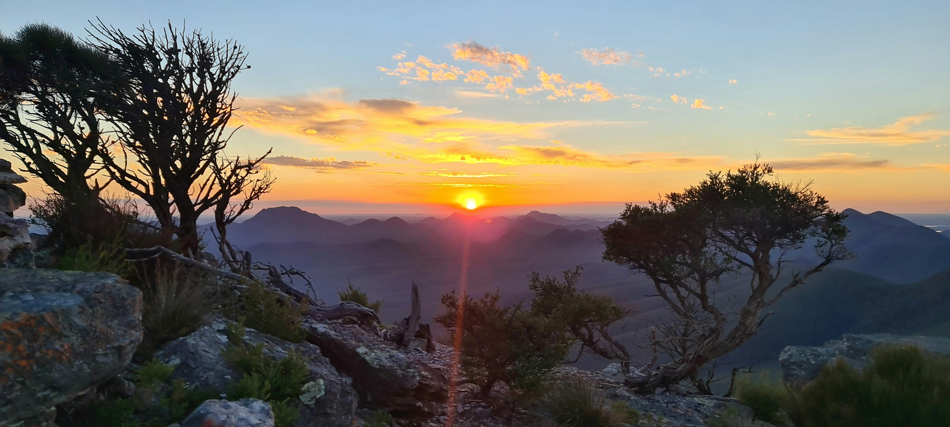 Warm orange sun rising in orange, purple and blue vibrant sky through layers of mountain peeks