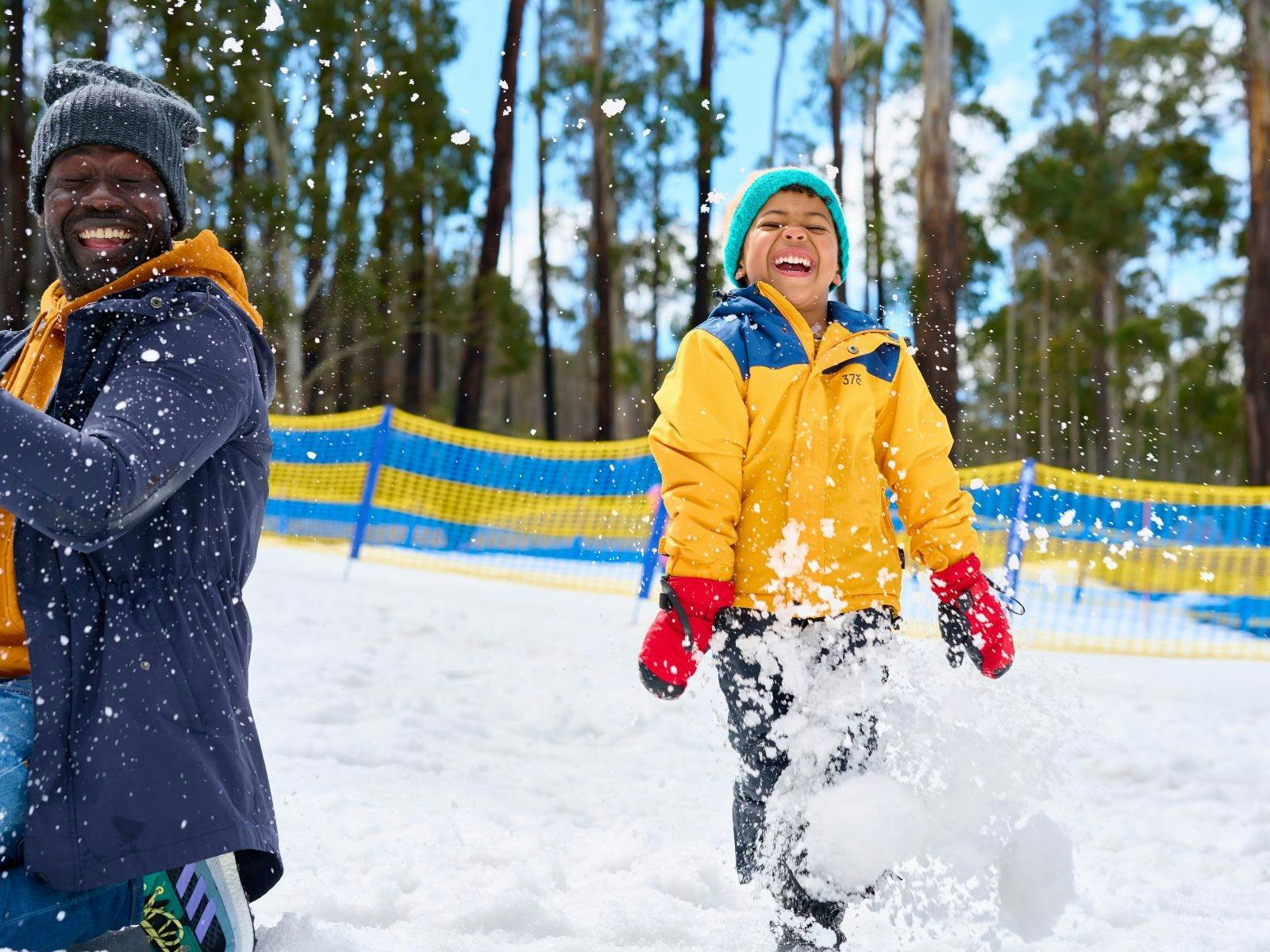 Father and son playing in the snow. Snow is sparaying around them as they laugh.