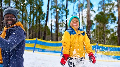 Father and son playing in the snow. Snow is sparaying around them as they laugh.