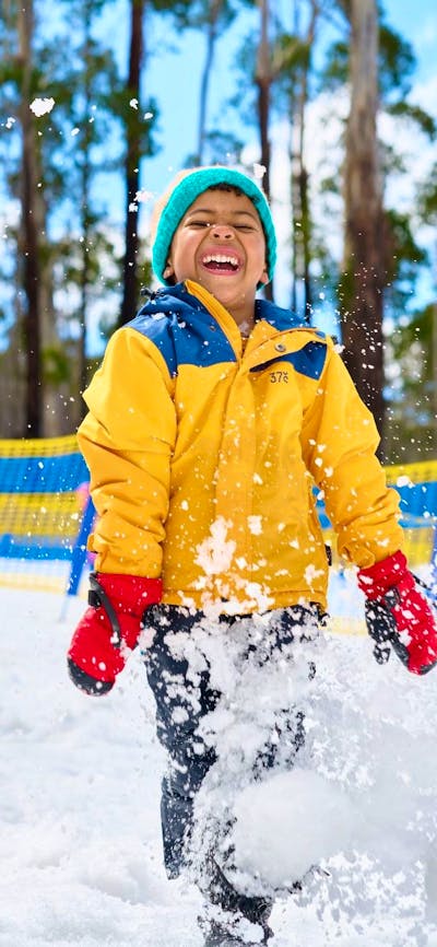 Father and son playing in the snow. Snow is sparaying around them as they laugh.