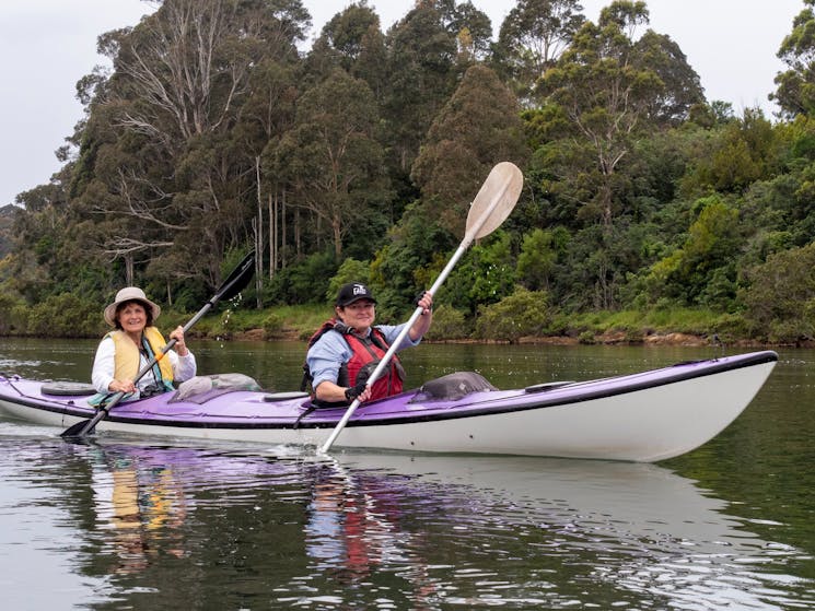 Two kayakers smile as they paddle the Bermagui River