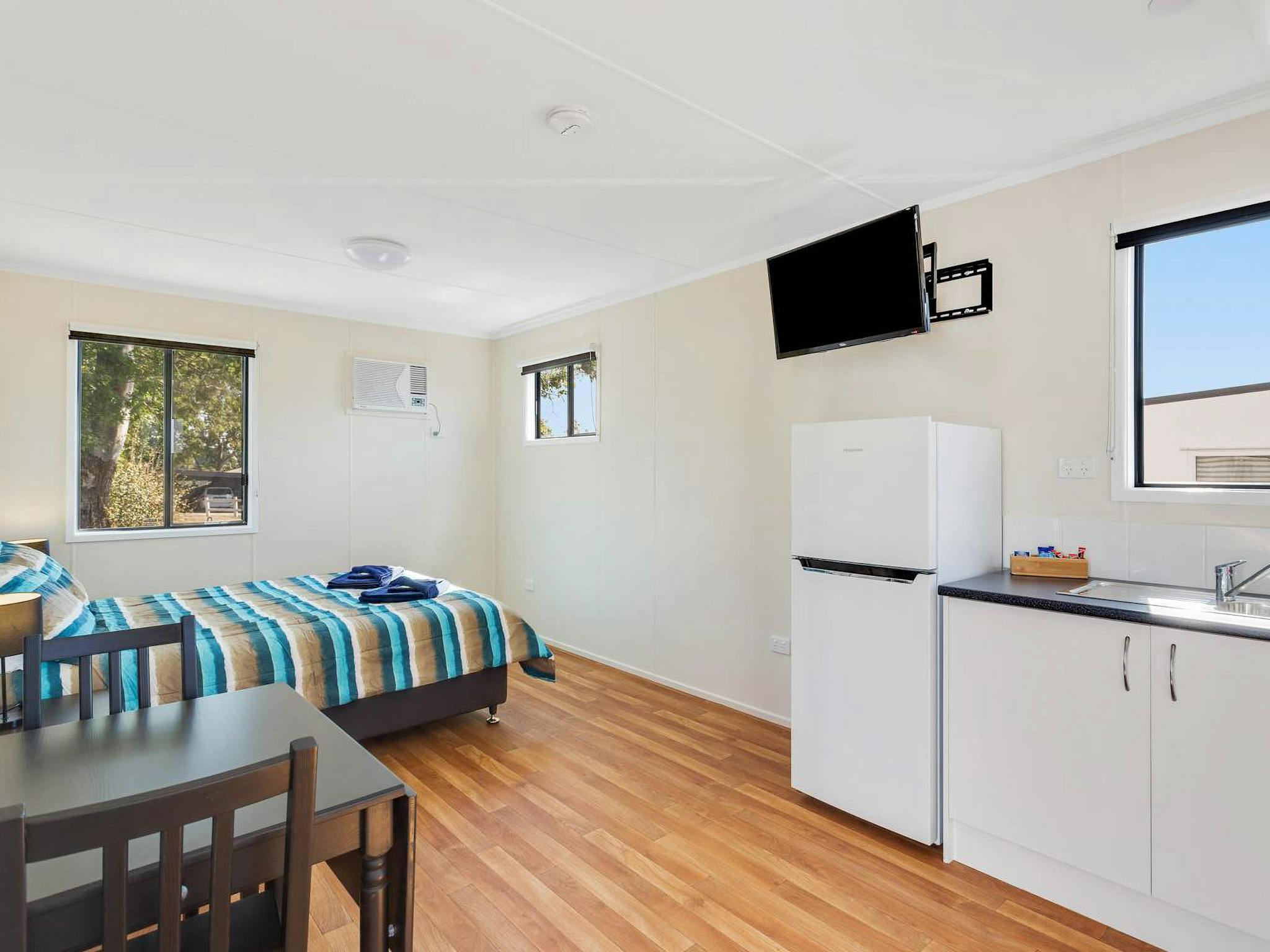 Open plan Deluxe Cabin interior with queen bed, kitchenette, dining table and timber flooring. Open plan Deluxe Cabin interior with queen bed, kitchenette, dining table and timber flooring.