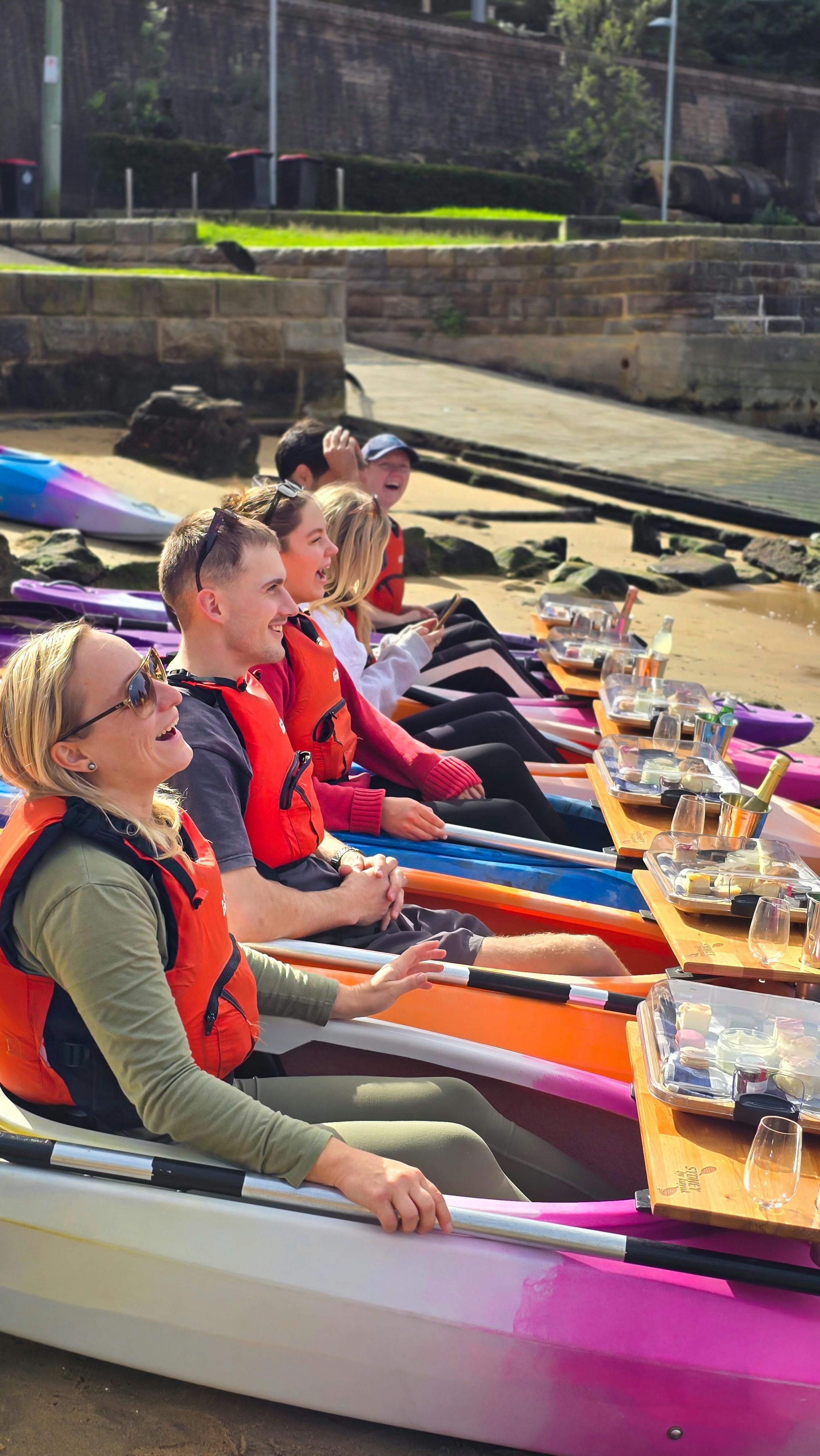 Guests lined in a row sitting in their kayaks on the beach listening to the briefing with smiles