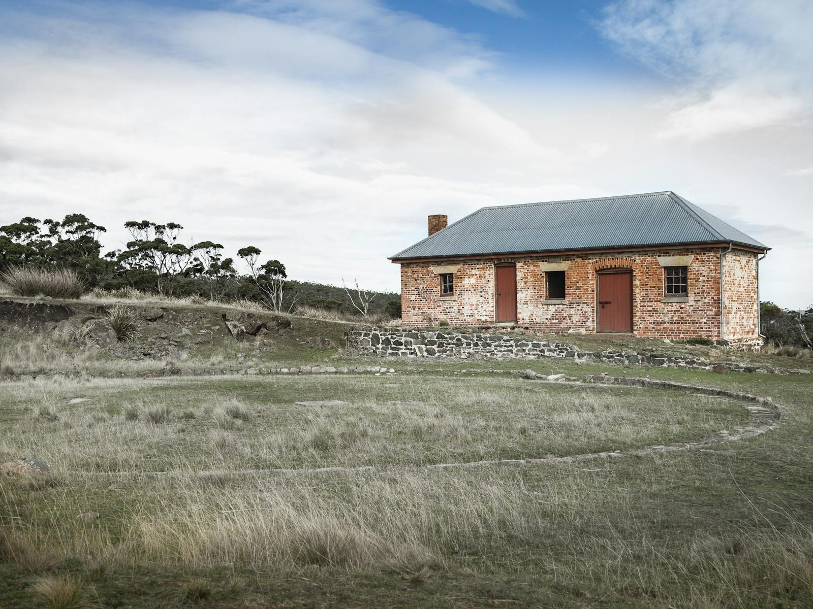 Colonial house (mill house) on sloping hill with dry grass around