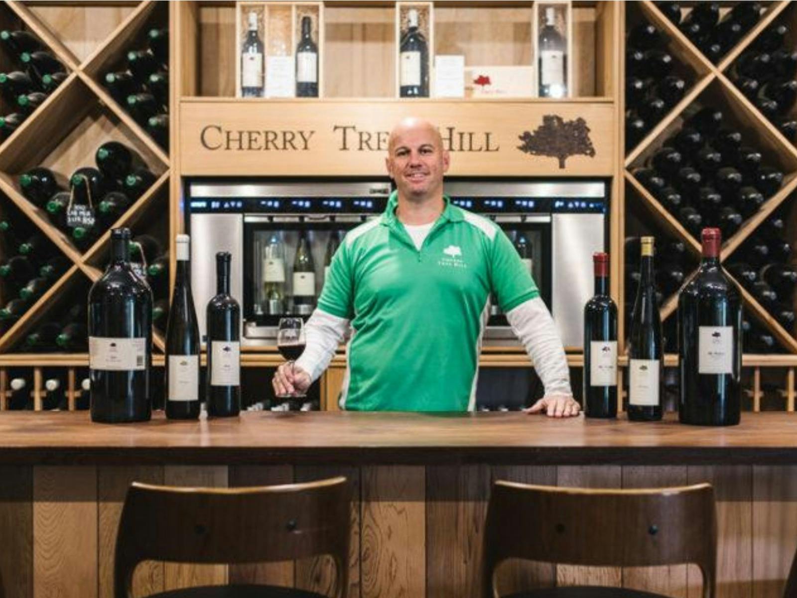 Man behind bar with bottles of wine on the bar and behind him