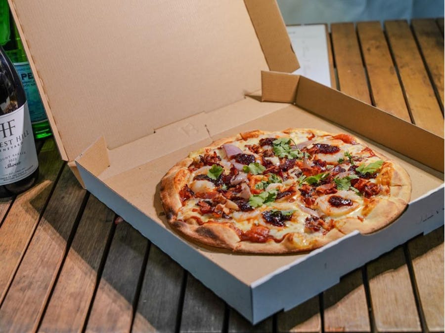 Takeaway chilli prawn pizza with red onion, bacon and coriander in a carboard box