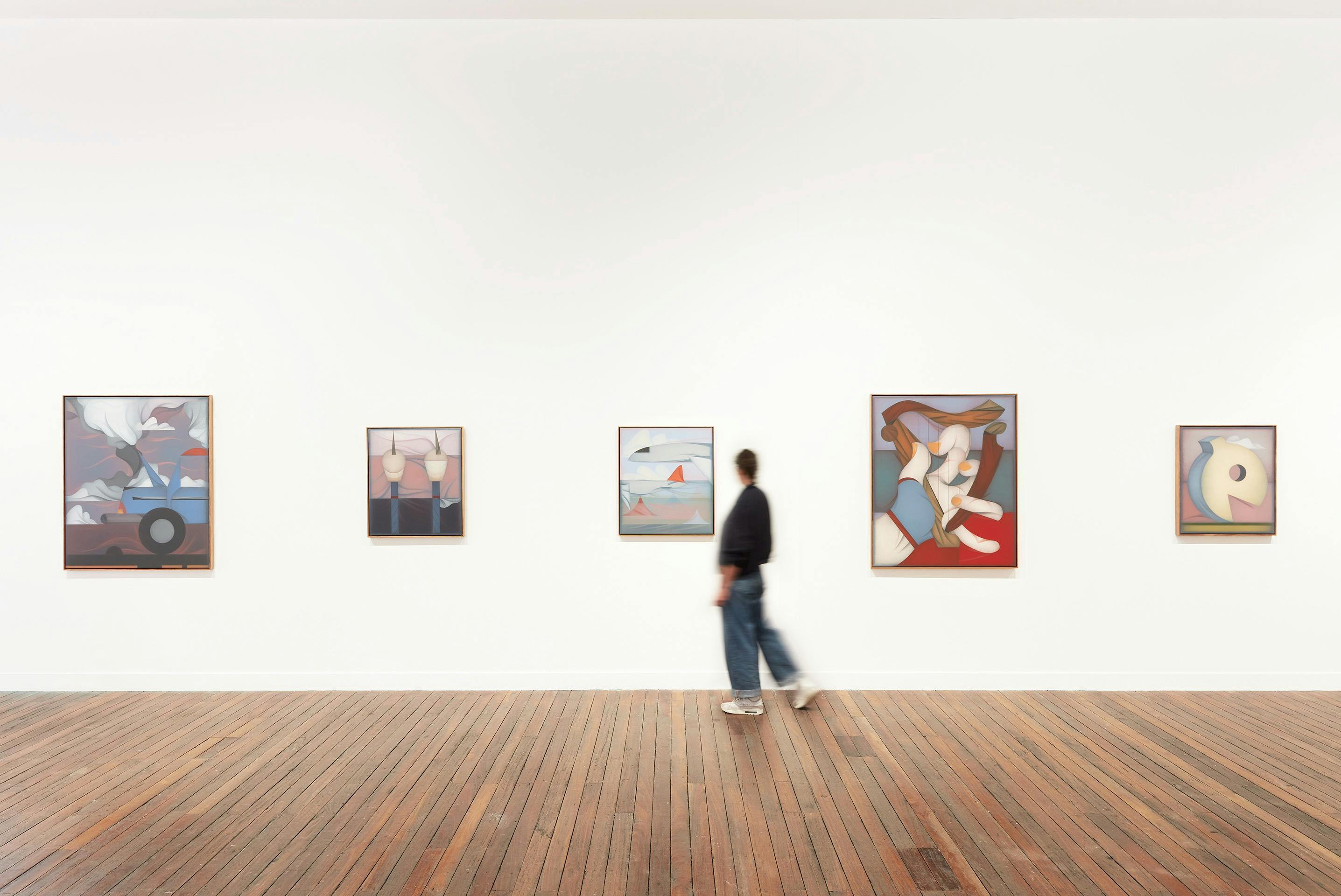 Person in gallery walking past paintings.