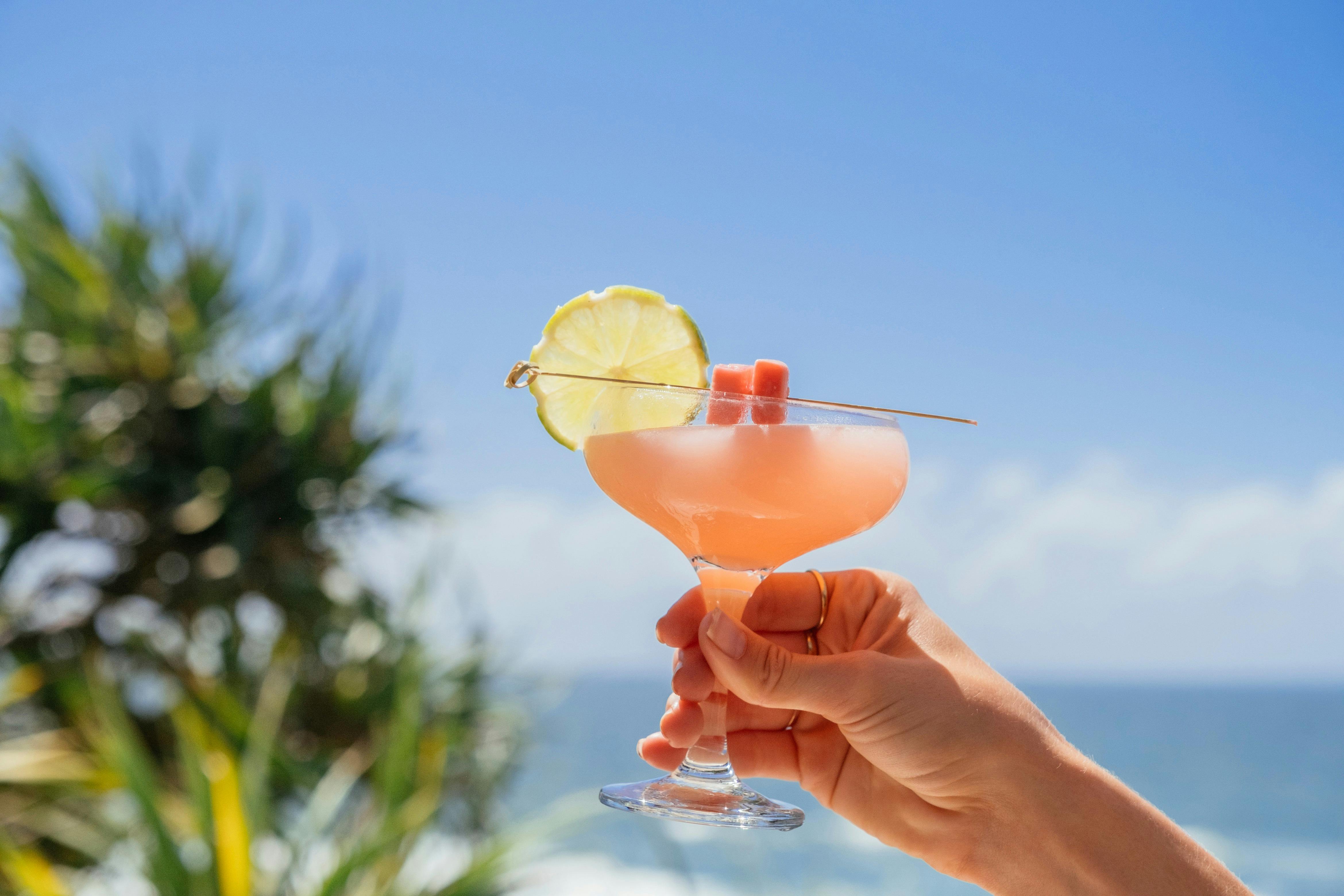 Hand holding a cocktail with a backdrop of the ocean and sky