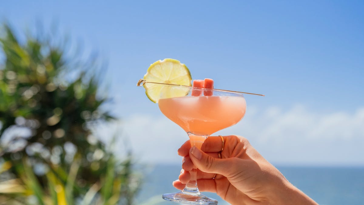 Hand holding a cocktail with a backdrop of the ocean and sky