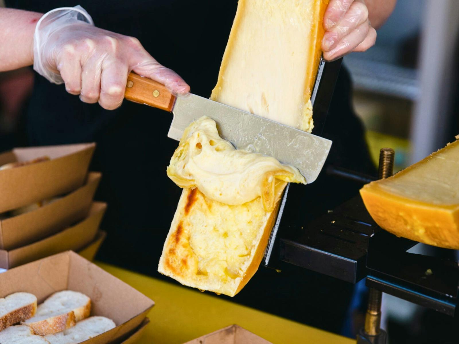 Melting cheese being scraped onto a bed of potatoes