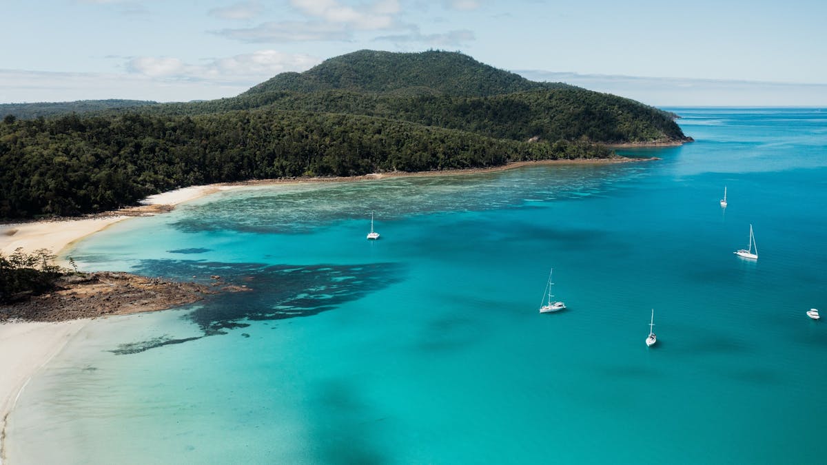 Aerial view of chance bay with sailing boats close to the beach and island hill covered in trees.