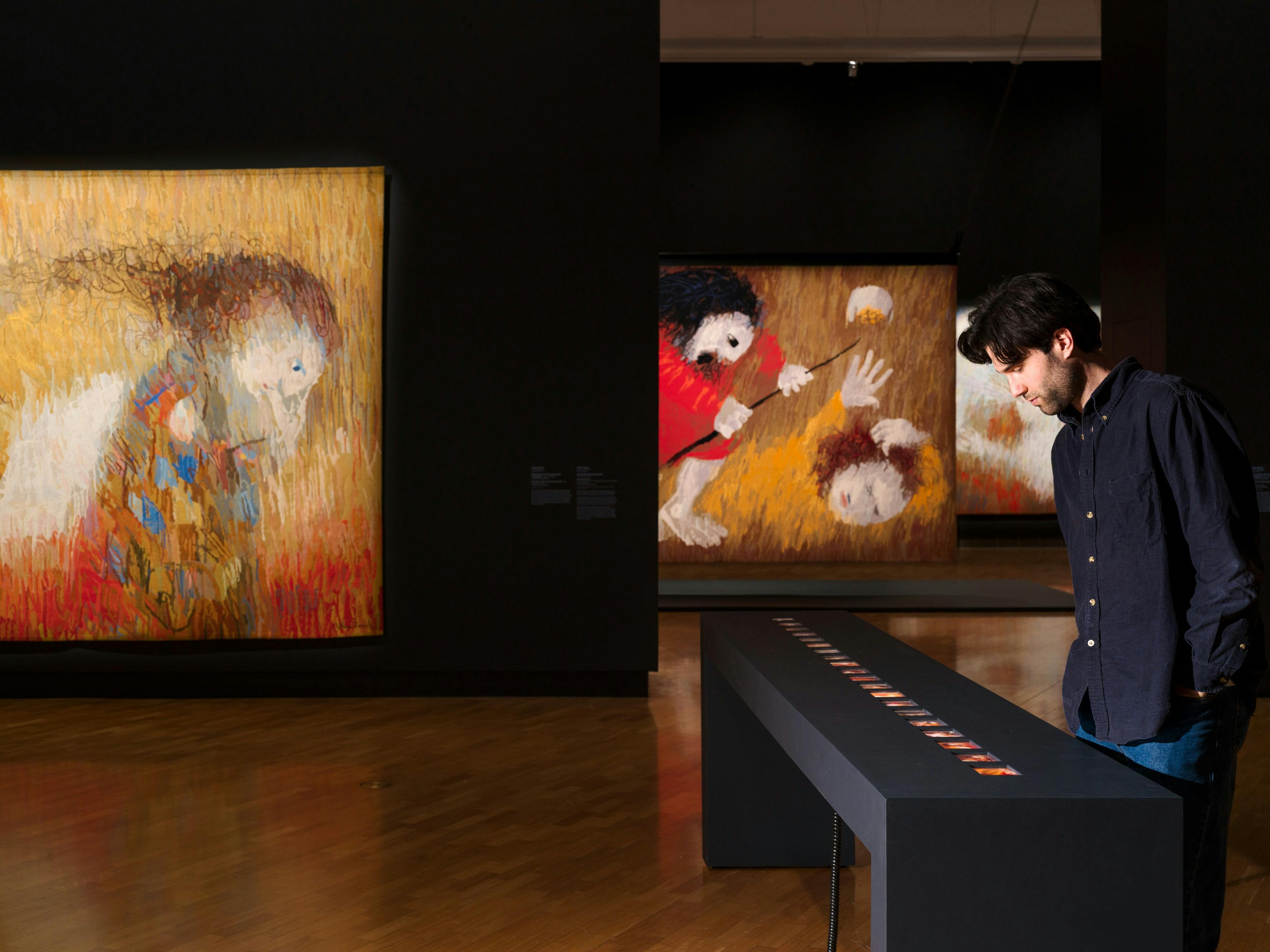 View of inside art exhibition with large tapestry and a visitor