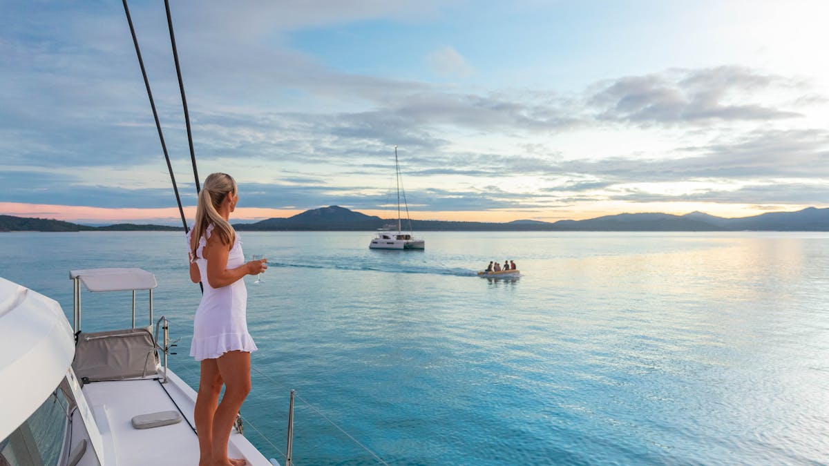Woman standing on deck watching a dinghy drive by.