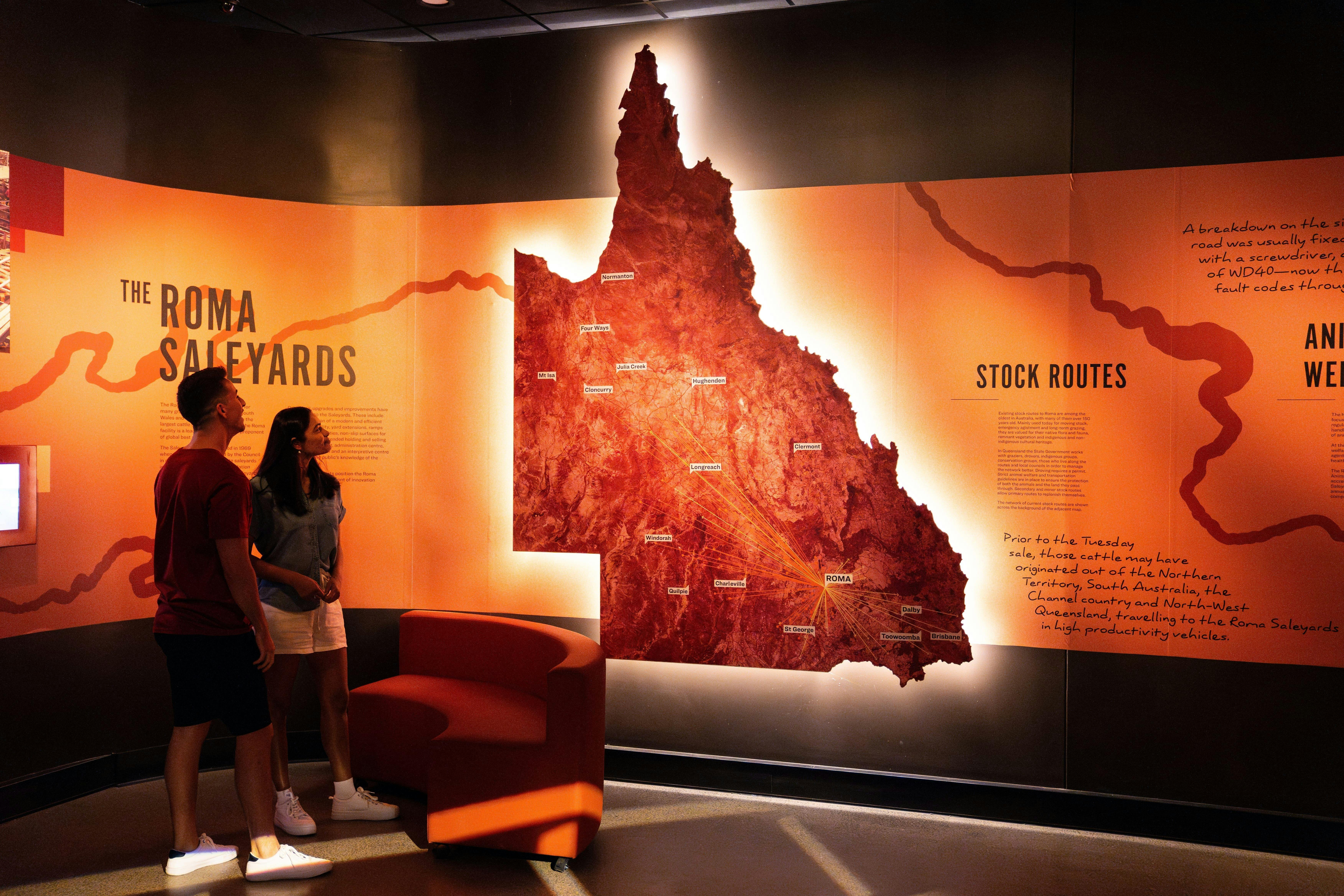 A couple in a dark room, looking at an illuminated map of Queensland showing stock routes