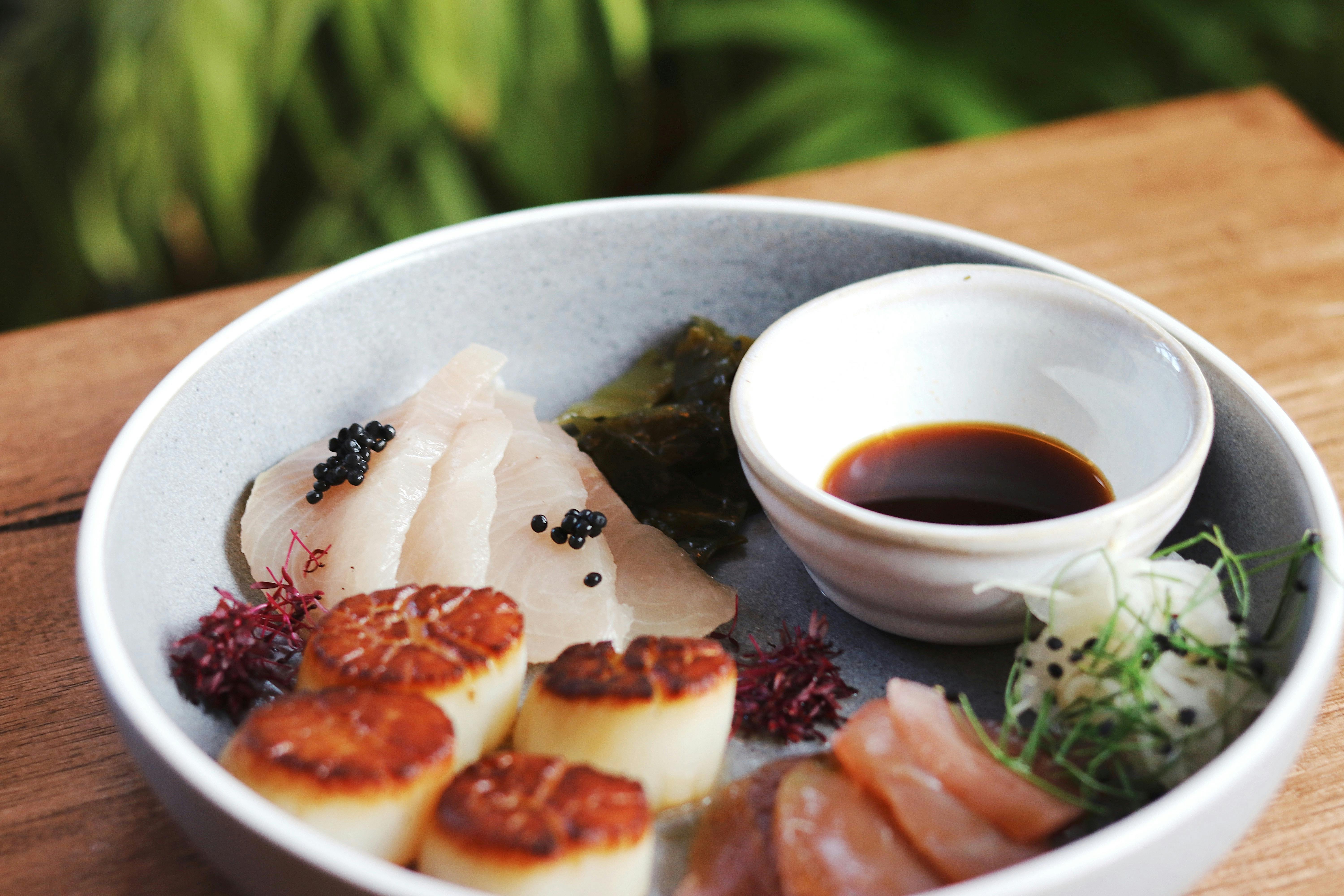A bowl features scallops, kingfish, ocean trout with a small bowl of ponzu sauce