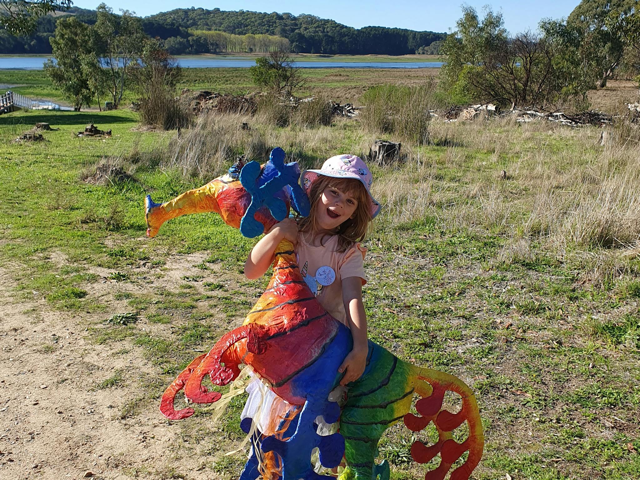 A young girl holding a large model of a colourful leaft sea dragon in a park like setting