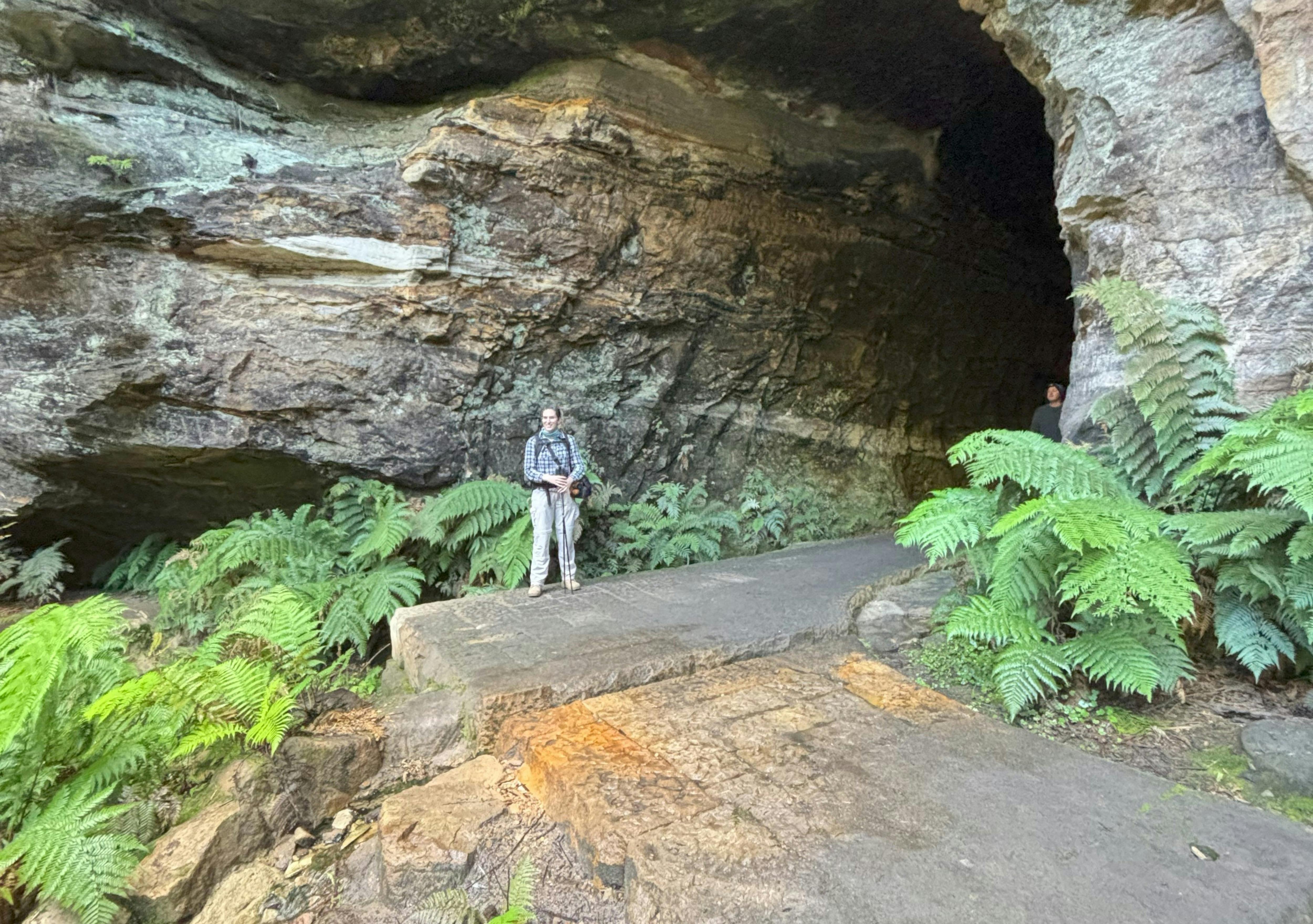 Woman standing at the entrance to a large tunnel carved into a sandstone cliff face.