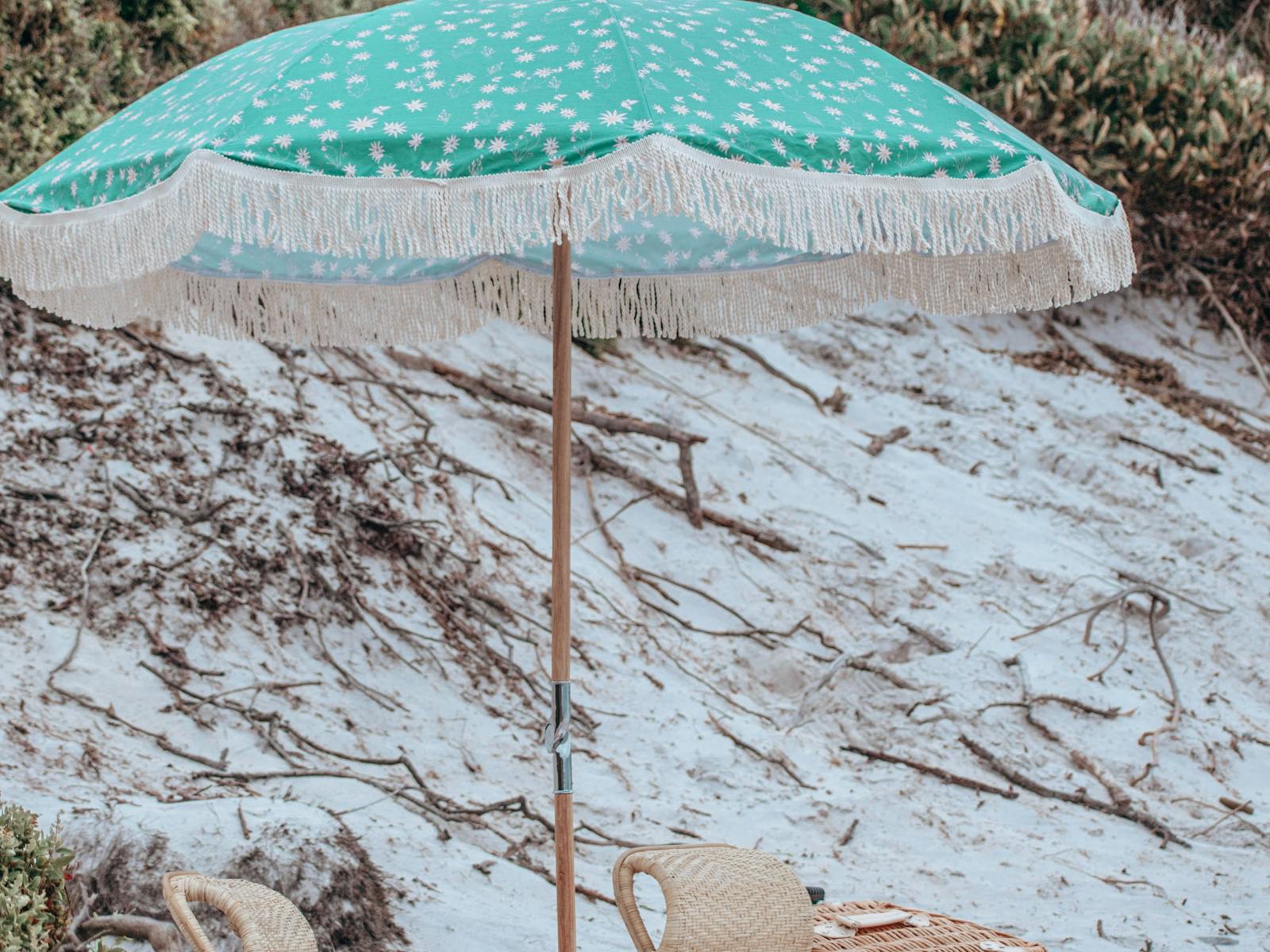 Aqua beach umbrella is set up above a beach picnic on a white sandy Tasmanian beach