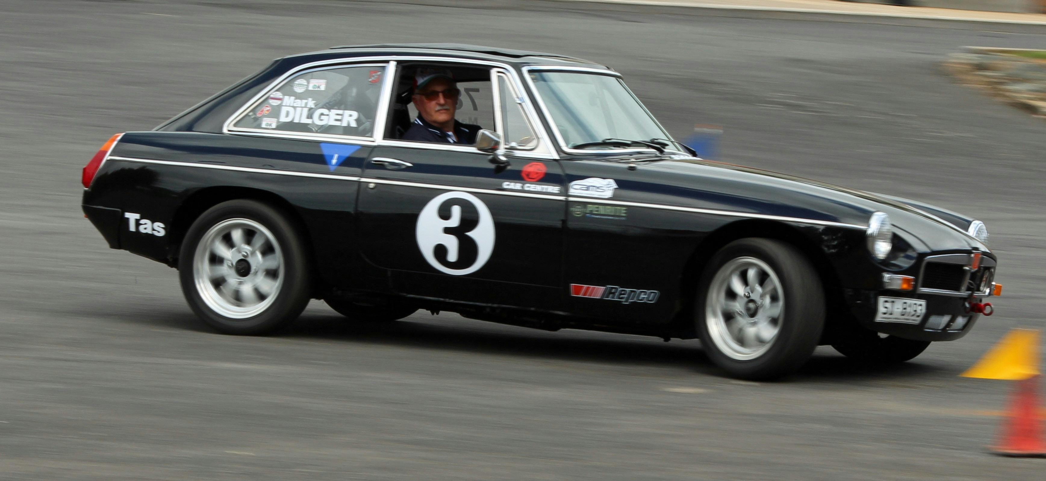 A black MG car in motion on a track, the background is a blur