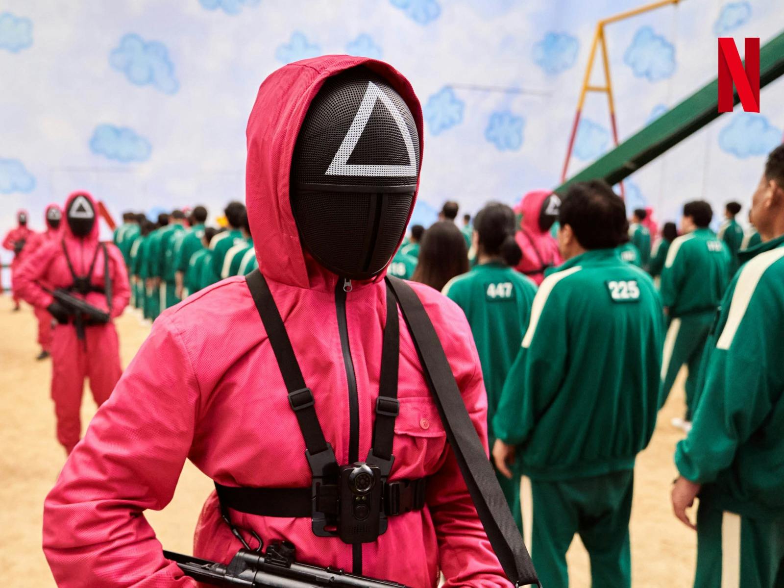 A still shot from movie Squid Game. Men in pink and green suits.