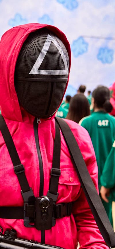 A still shot from movie Squid Game. Men in pink and green suits.