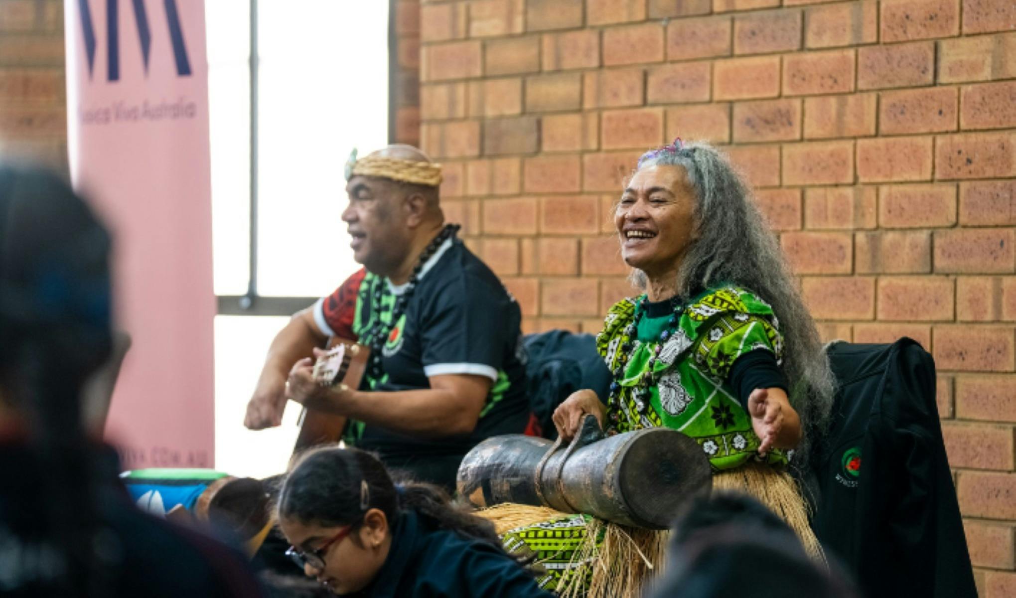 2 performers play music for an audience, one playing a guitar and one playing percussion instrument