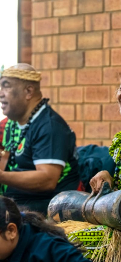 2 performers play music for an audience, one playing a guitar and one playing percussion instrument