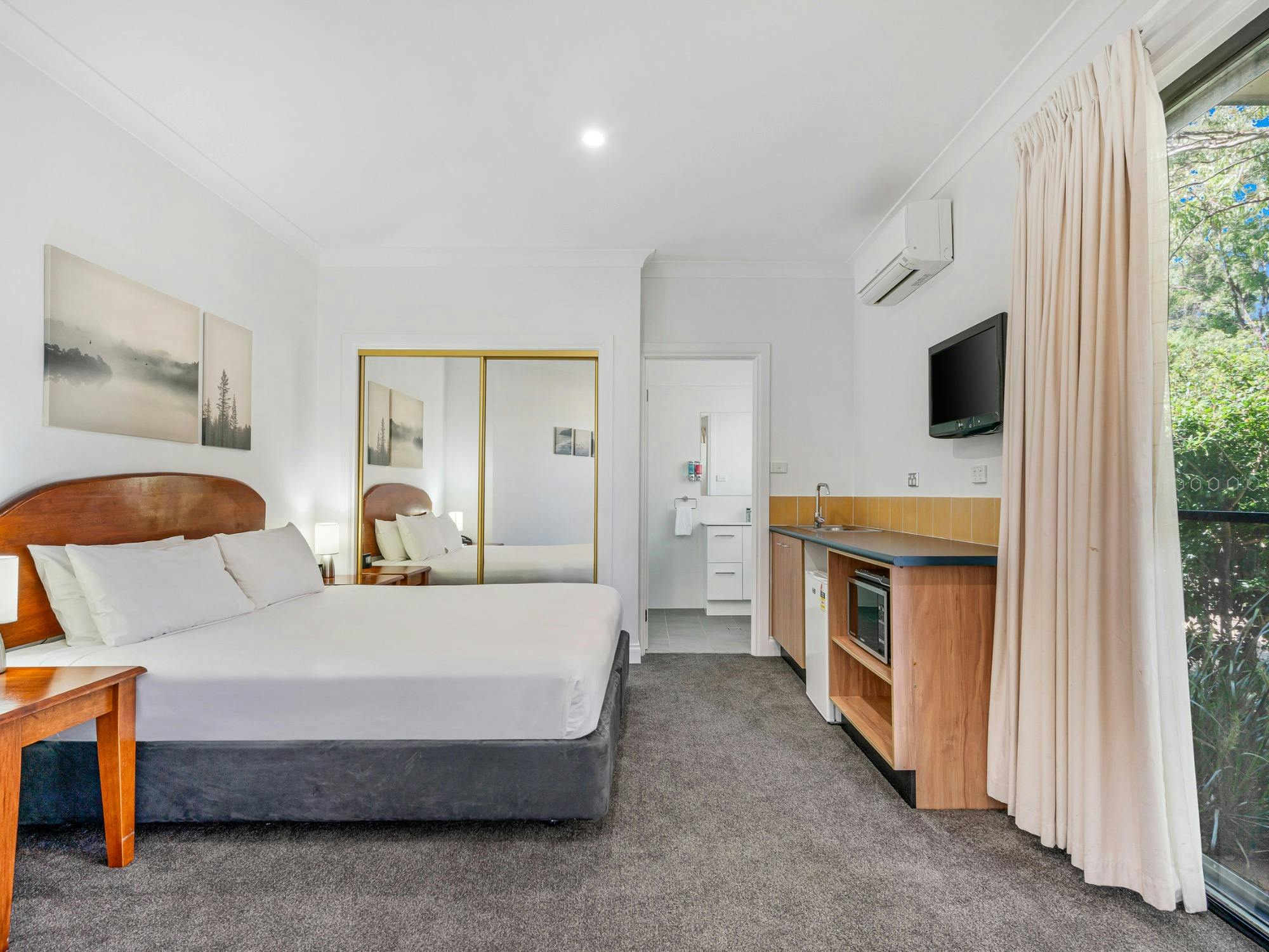 Studio room with queen bed, kitchenette, TV and sliding door to outdoor area