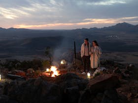 Couple on a heli-camping experience having dinner cooked over a firepit on Chace Range
