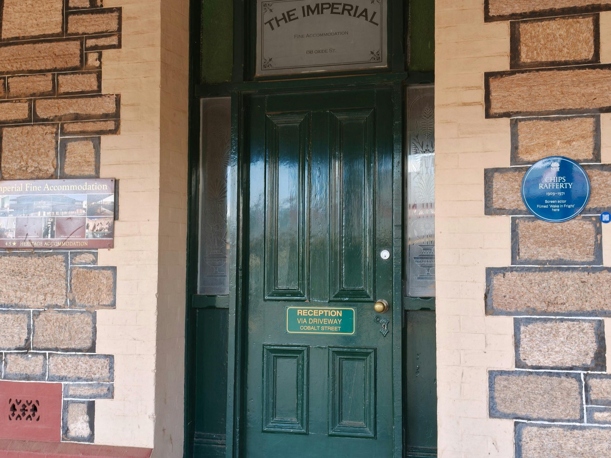 Blue plaque on wall next to green door with "reception" sign and  transom window saying The Imperial