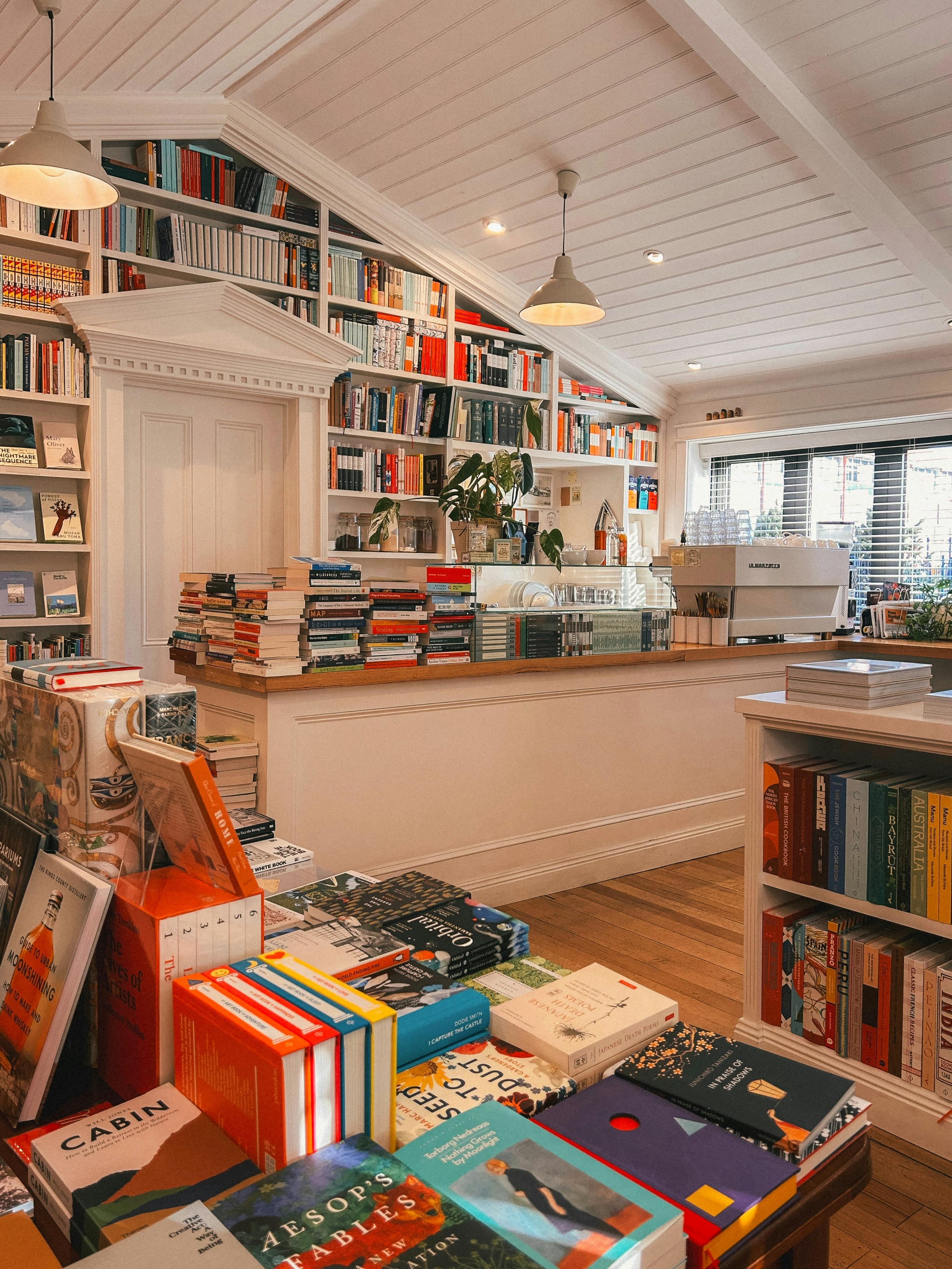 Books displayed on tables near a café counter and shelves in a bright bookshop.