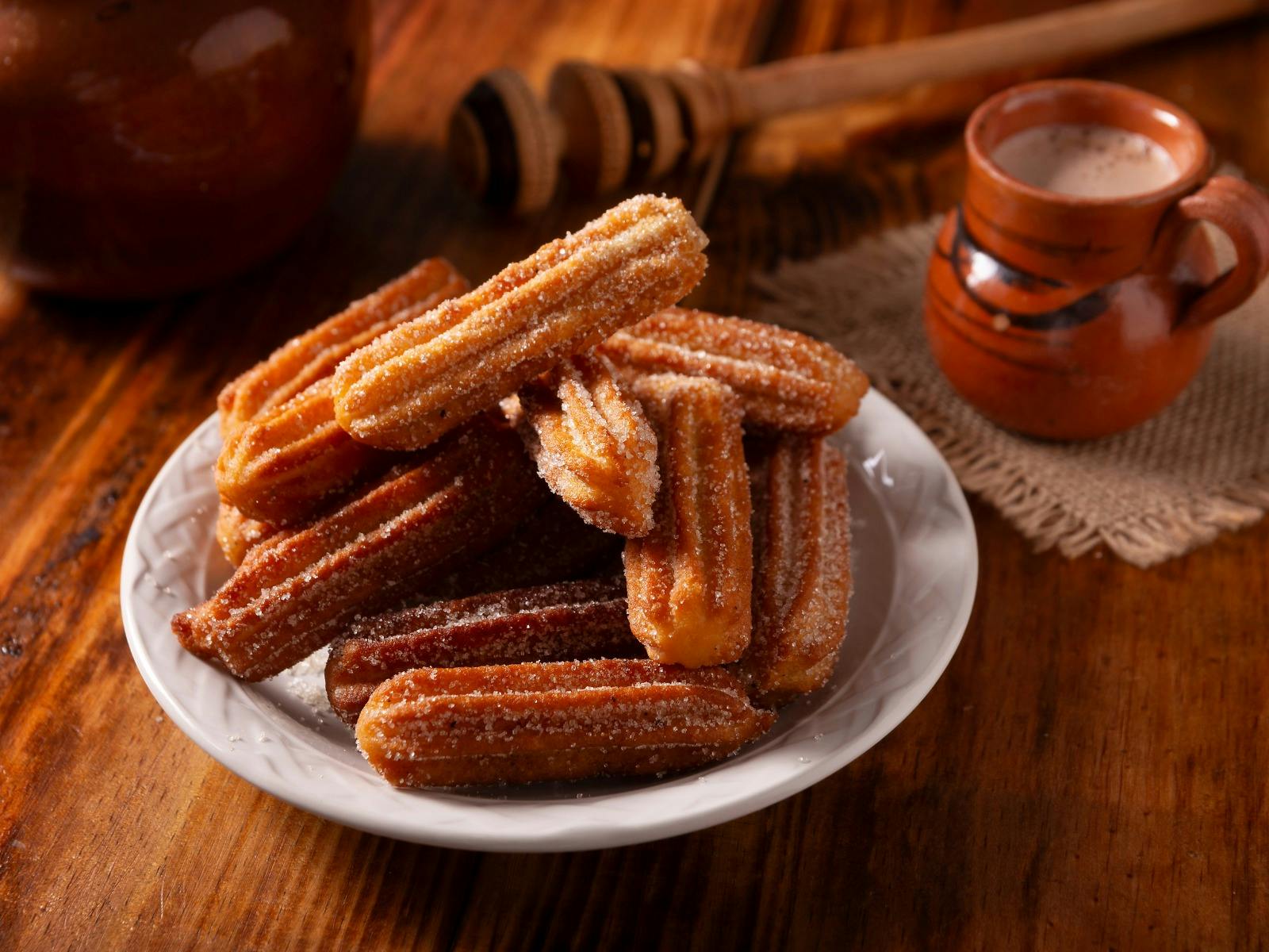 Dark and moody image of a plate of cripsy Churros with a side of dipping chocolate