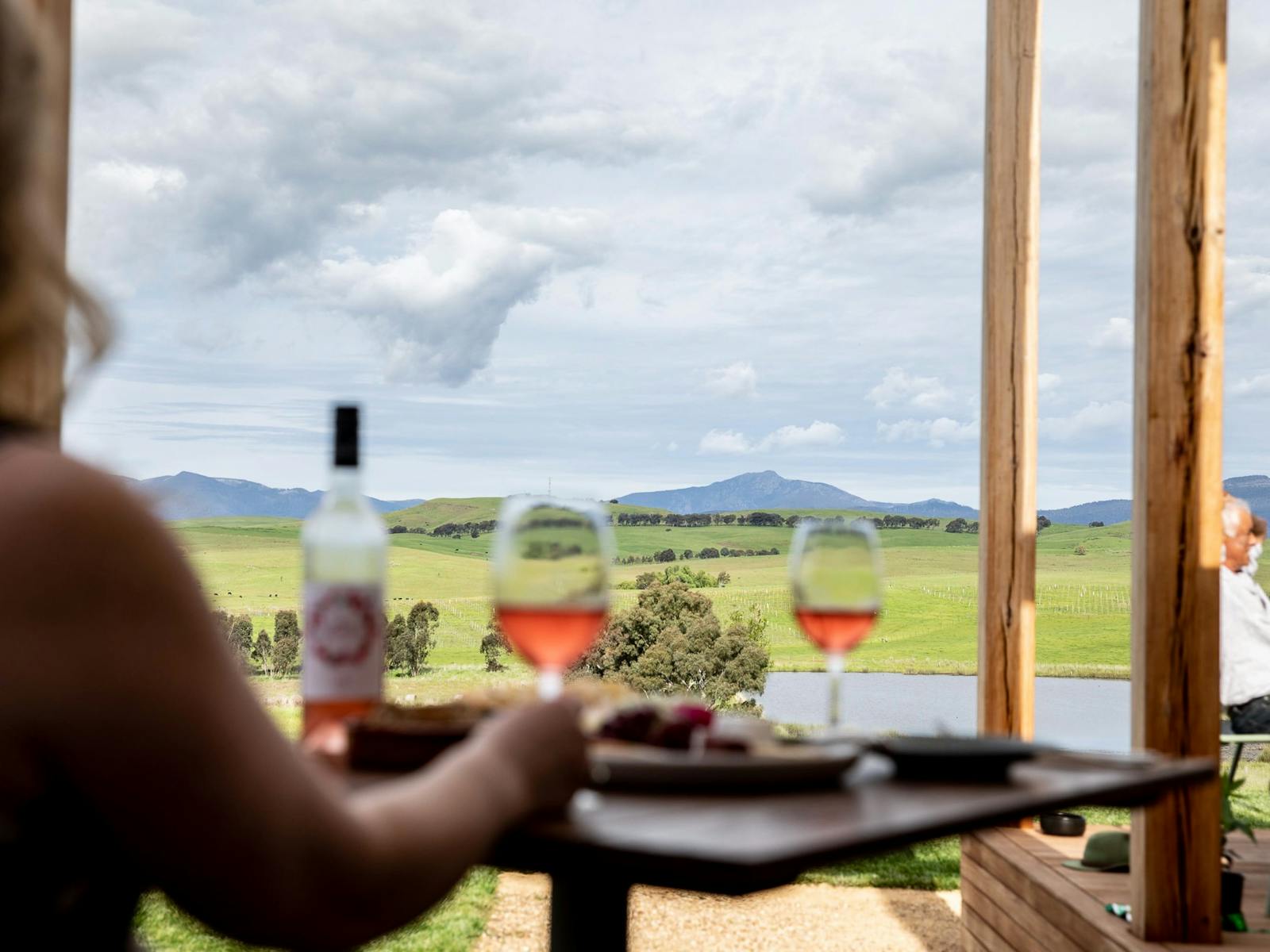 A table with two people, glasses of wine and a platter in front of a view of Mt Buller