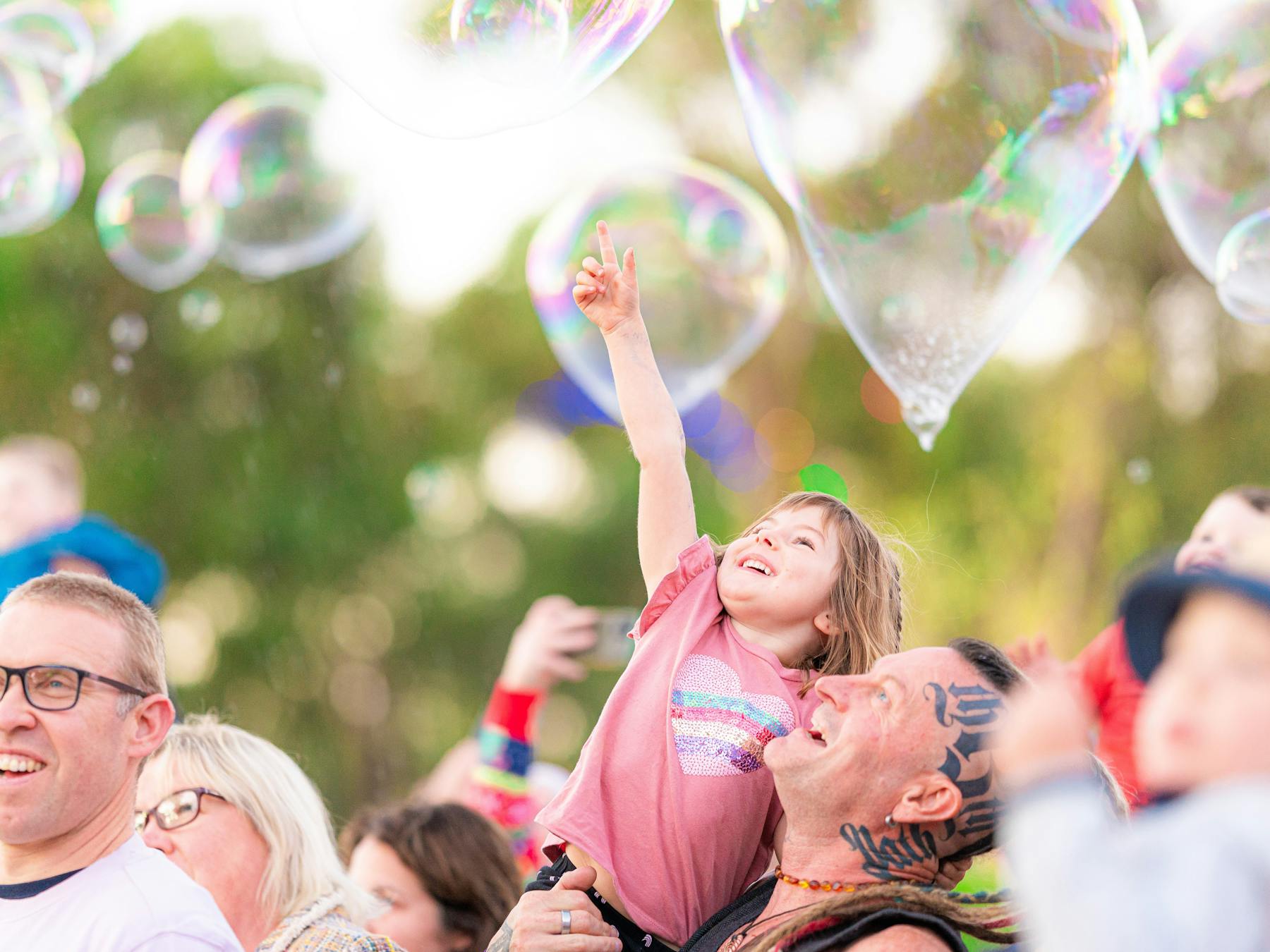 kid in pink shirt being lifted in air popping a large bubble