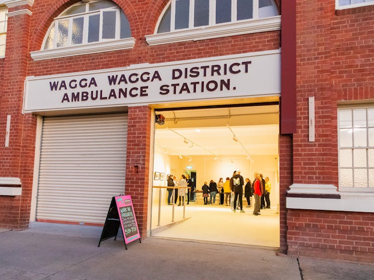 Photo of the front of old ambulance building, one roller door is raised to show event inside