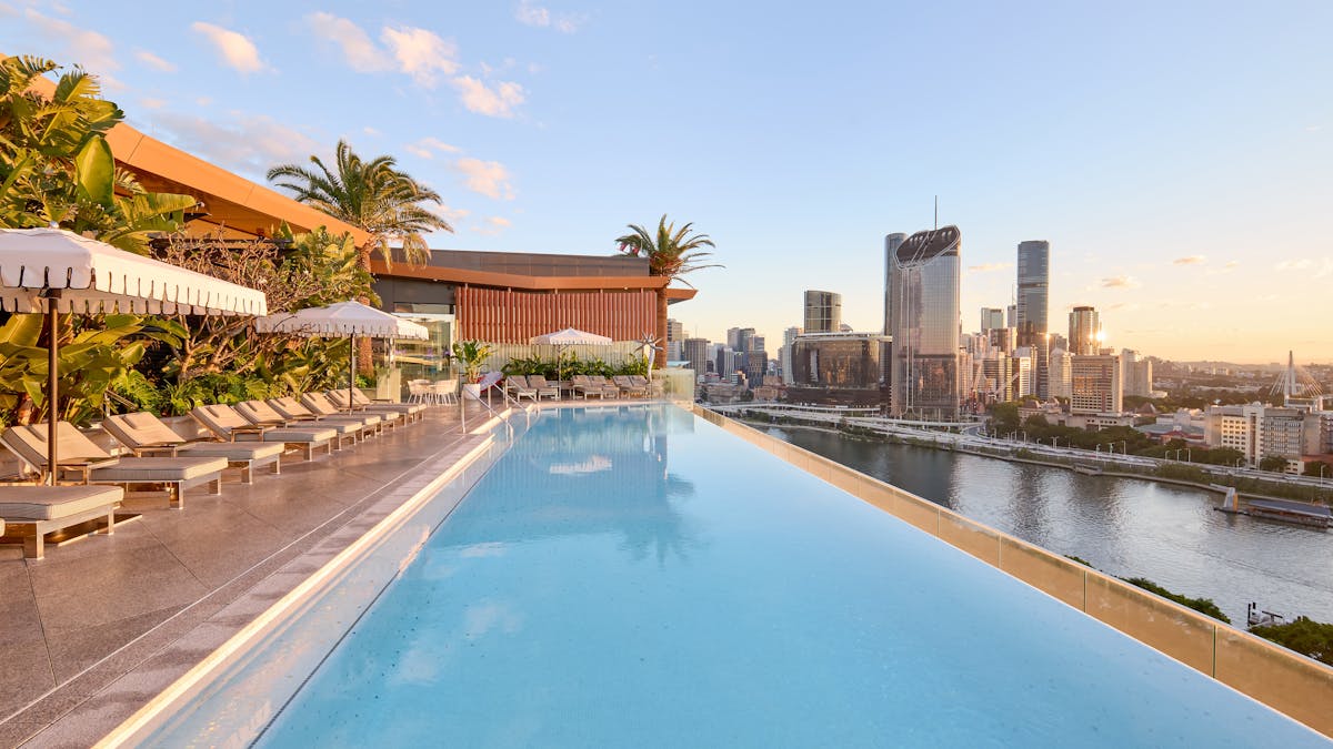 Rooftop infinity pool with sun loungers, umbrellas and panoramic views over Brisbane