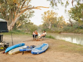 A couple sits in camp chairs beside their campervan on the banks of the Cooper Creek.