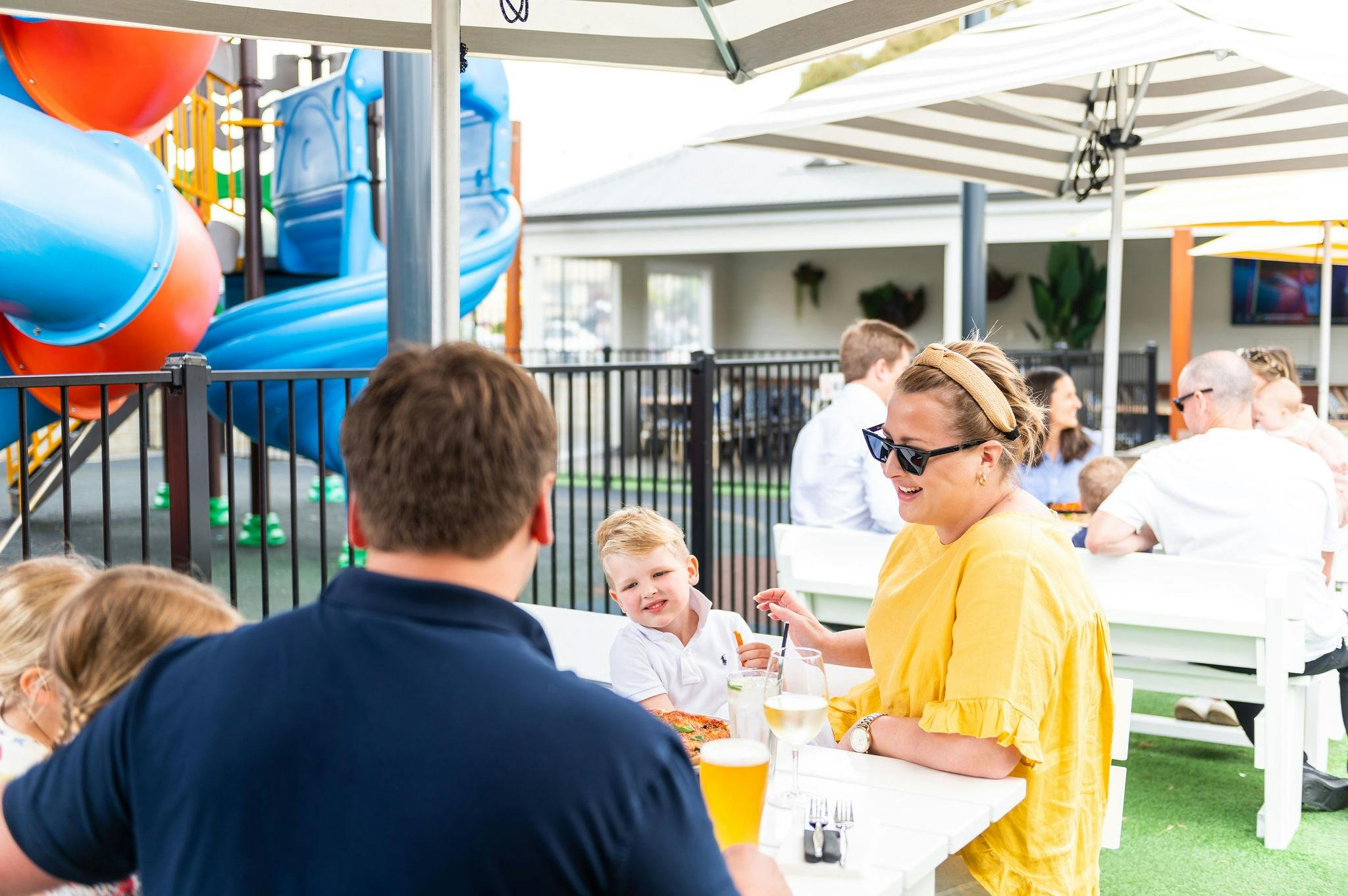Man in vay shirt, Woman in yellow shirt and two children dining in sunny beer garden